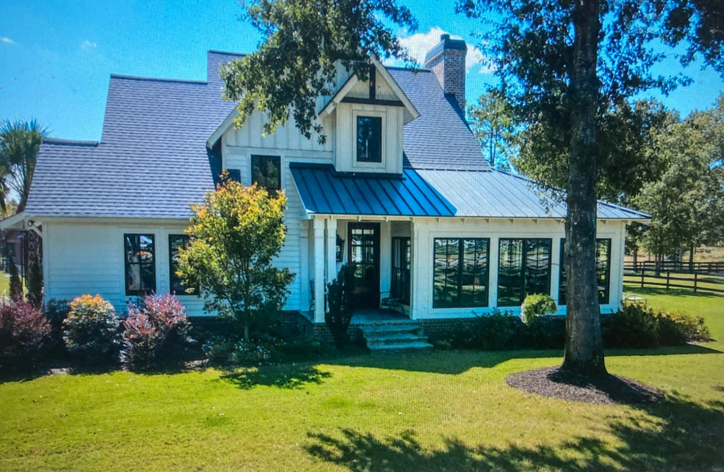 White country home with gabled roofs, dark-framed windows, mature trees and a lawn in Aiken, South Carolina