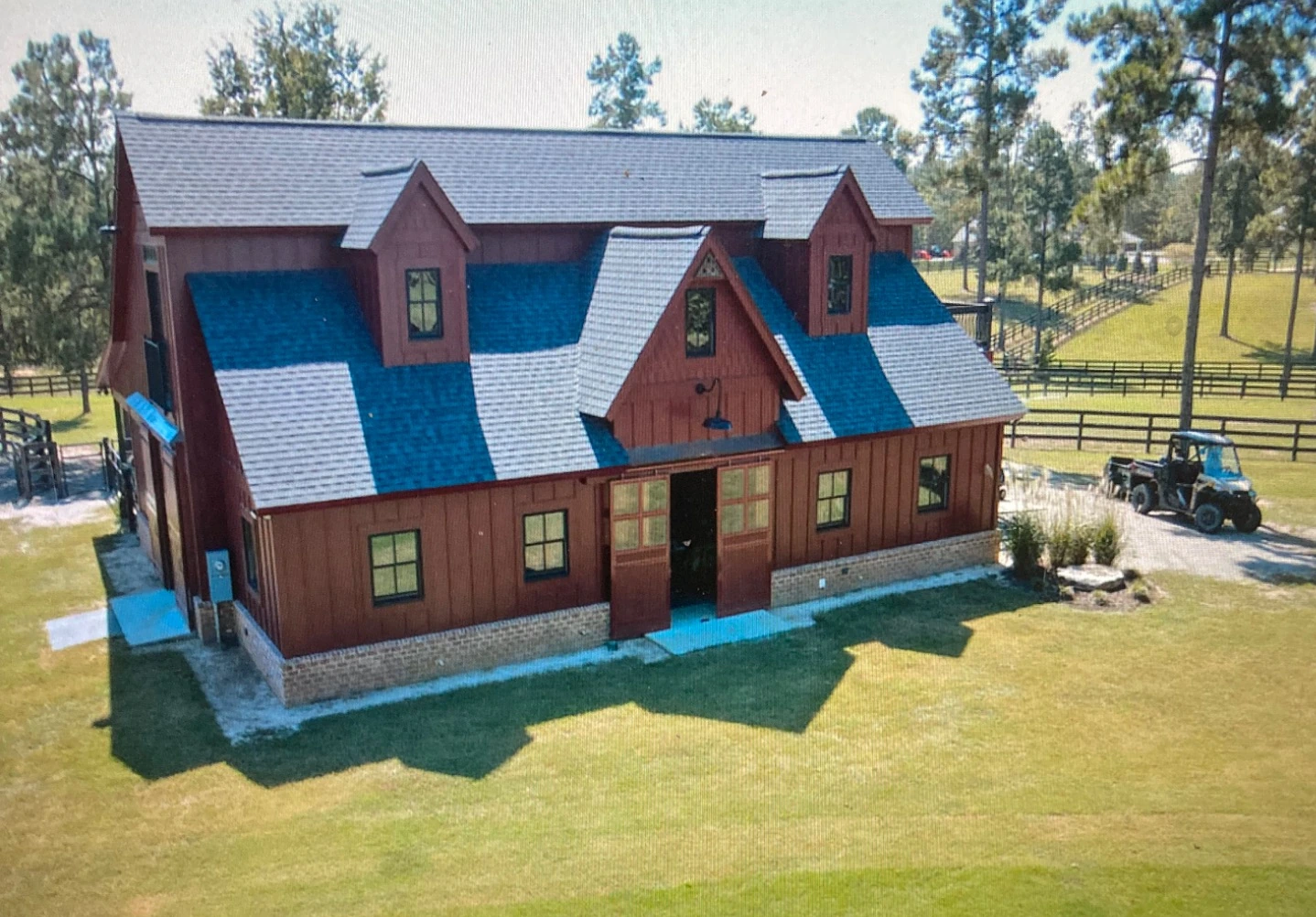 Red stable with dormer windows and a gray roof beside fenced paddocks in Aiken, South Carolina