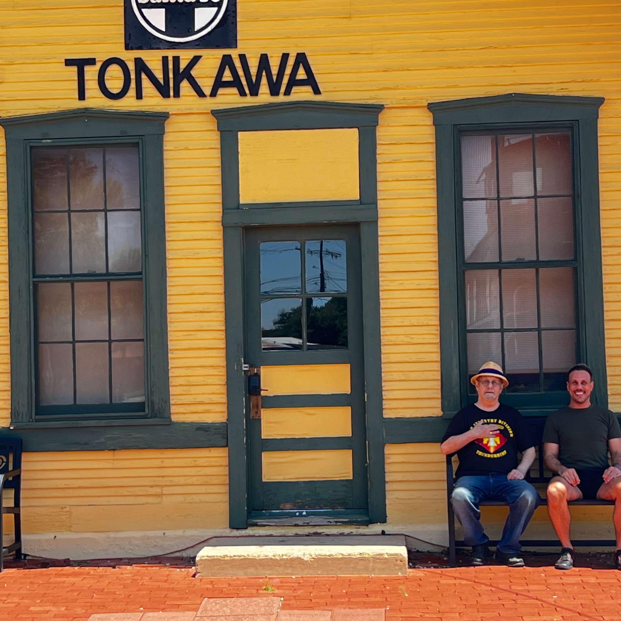 Jerry Lee Johnson and his son Nathan Johnson seated together outside the yellow Tonkawa depot