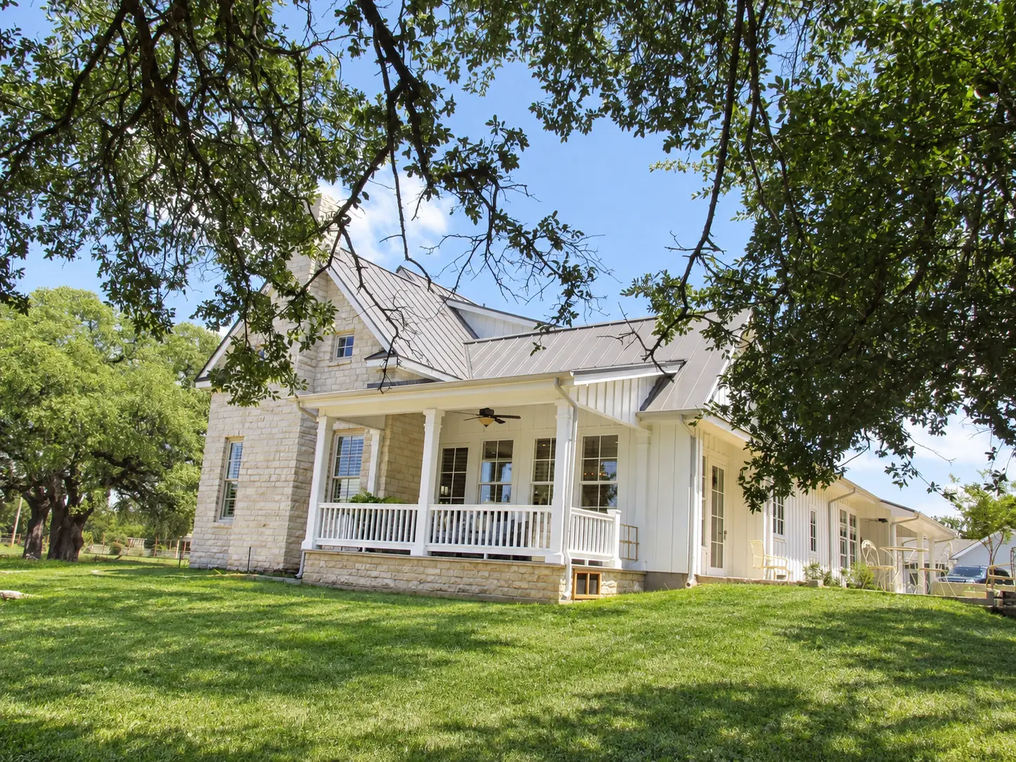 Covered farmhouse porch beneath mature shade trees