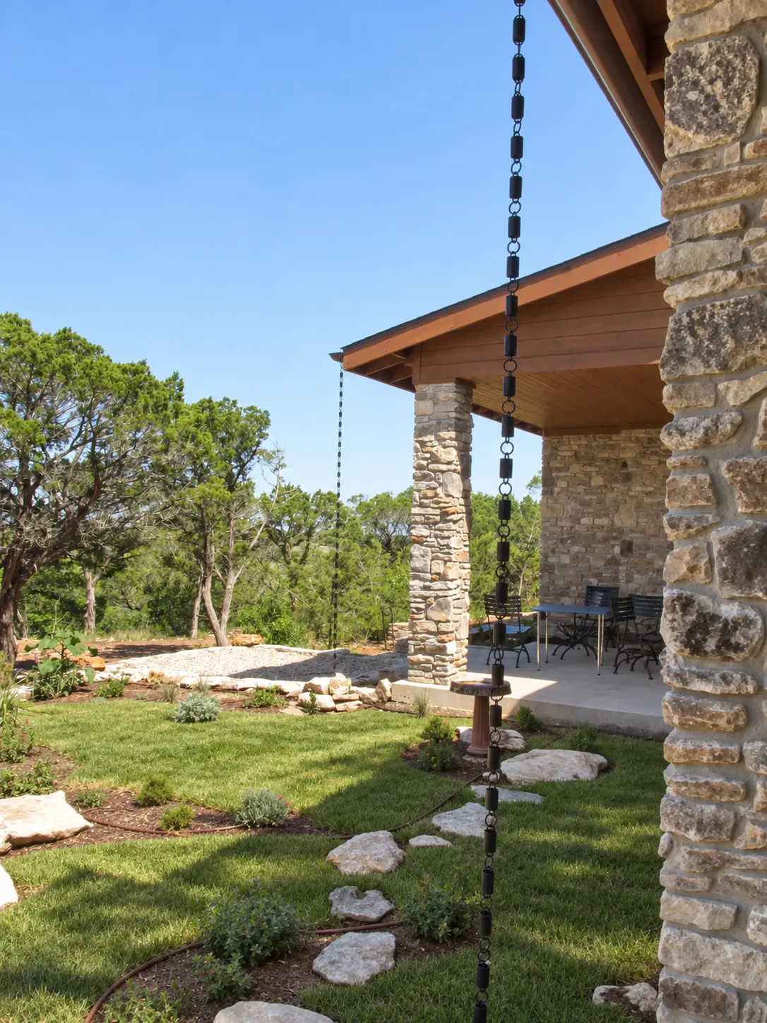 A covered terrace overlooking trees, with a stone column and rain chain