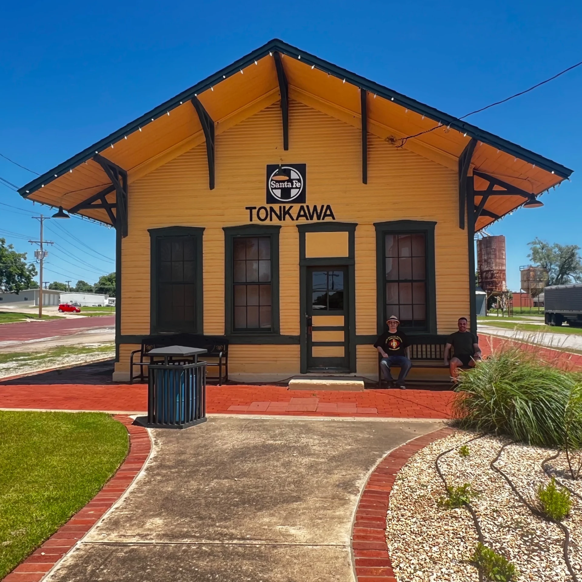 The yellow Tonkawa railway depot with dark green trim and a brick approach